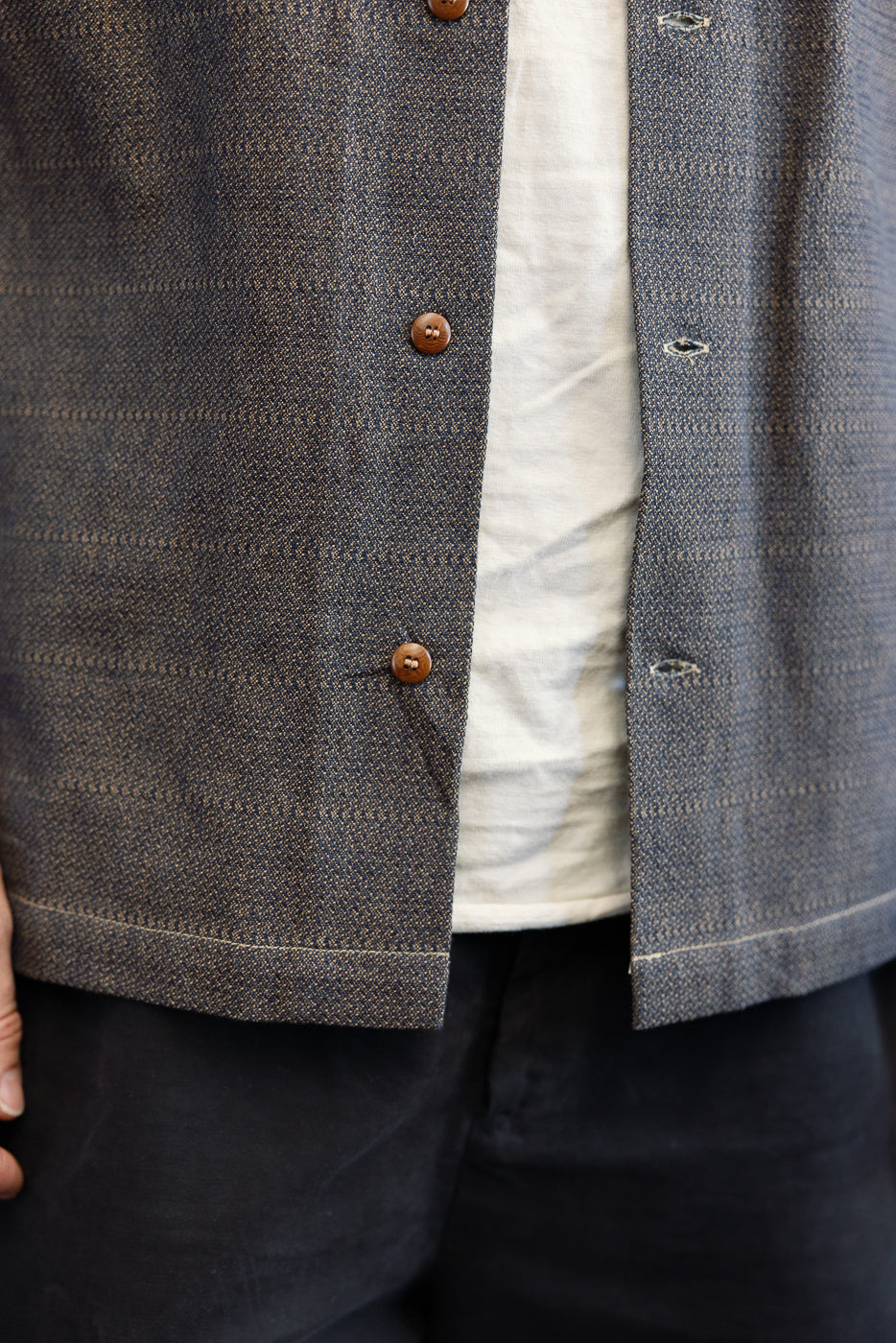 Close-up front view of men's plaid shirt with brown buttons, textured fabric, and hem detail on athletic build model