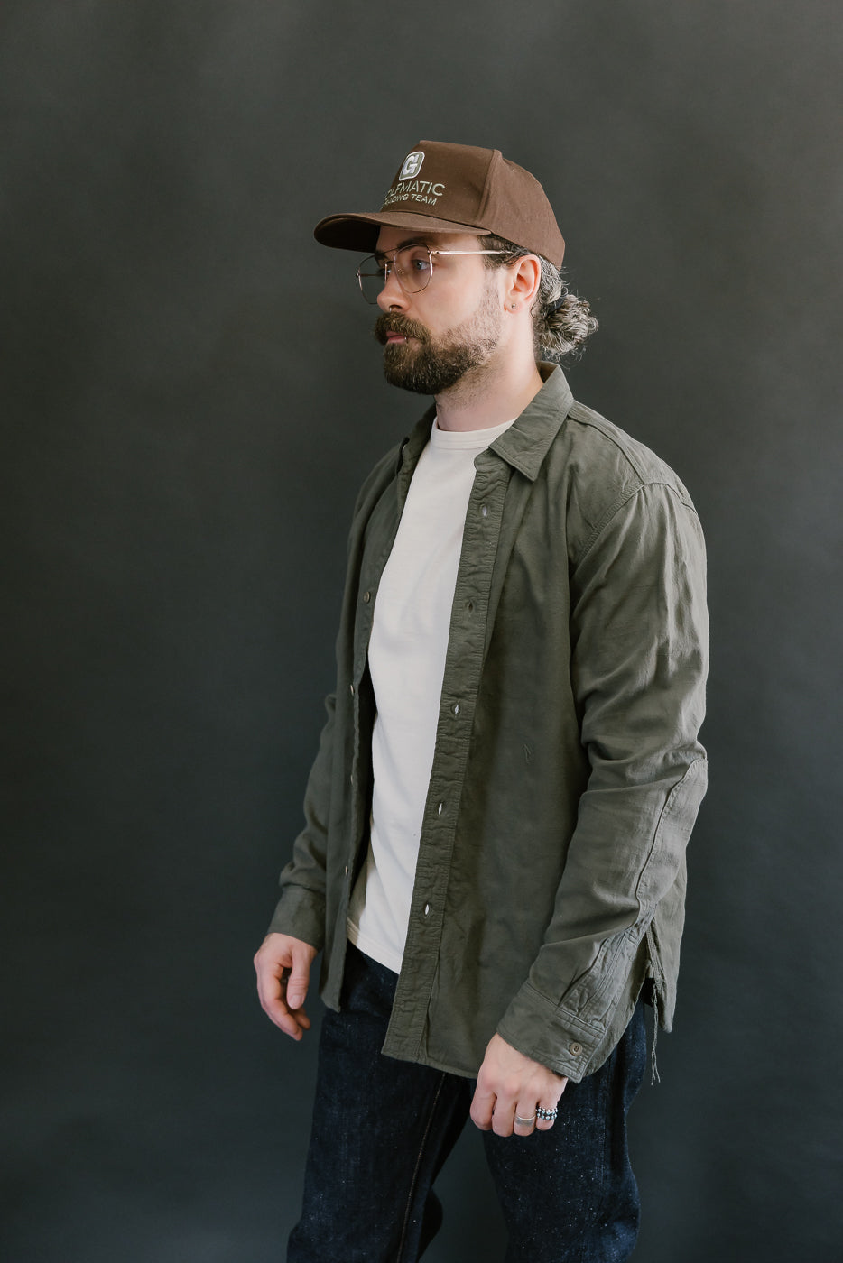 Man wearing SSS25-ATW Tropical Weather Dobby Shirt in olive green, showcasing its military-inspired style, buttoned cuffs, and textured Panama-weave fabric.