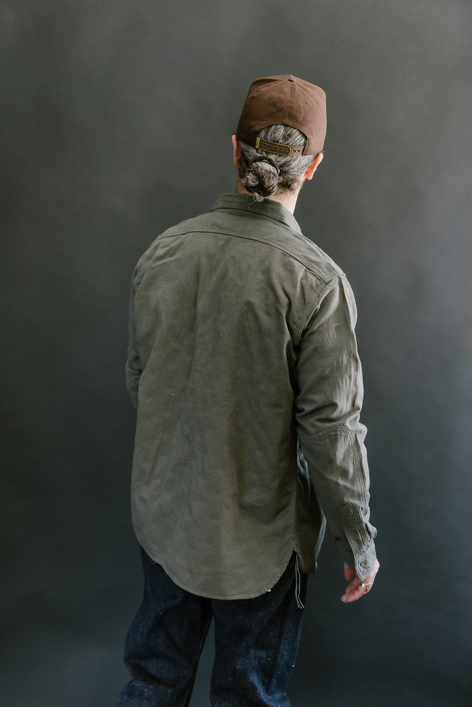 Person wearing the SSS25-ATW Tropical Weather Dobby Shirt in olive green, showcasing its Westerners Cut and durable design, including reinforced elbow patches and buttoned barrel cuffs.