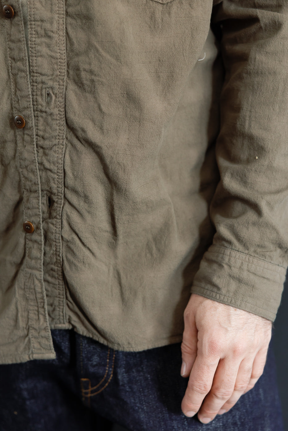 Close-up front view of olive shirt with brown buttons, worn by male model, 5'9
