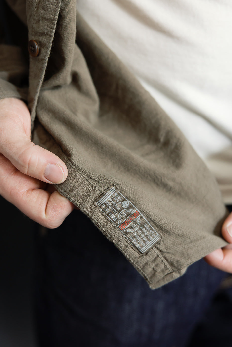 Close-up of olive shirt sleeve hem showing woven tag detail, worn by male model 5'9