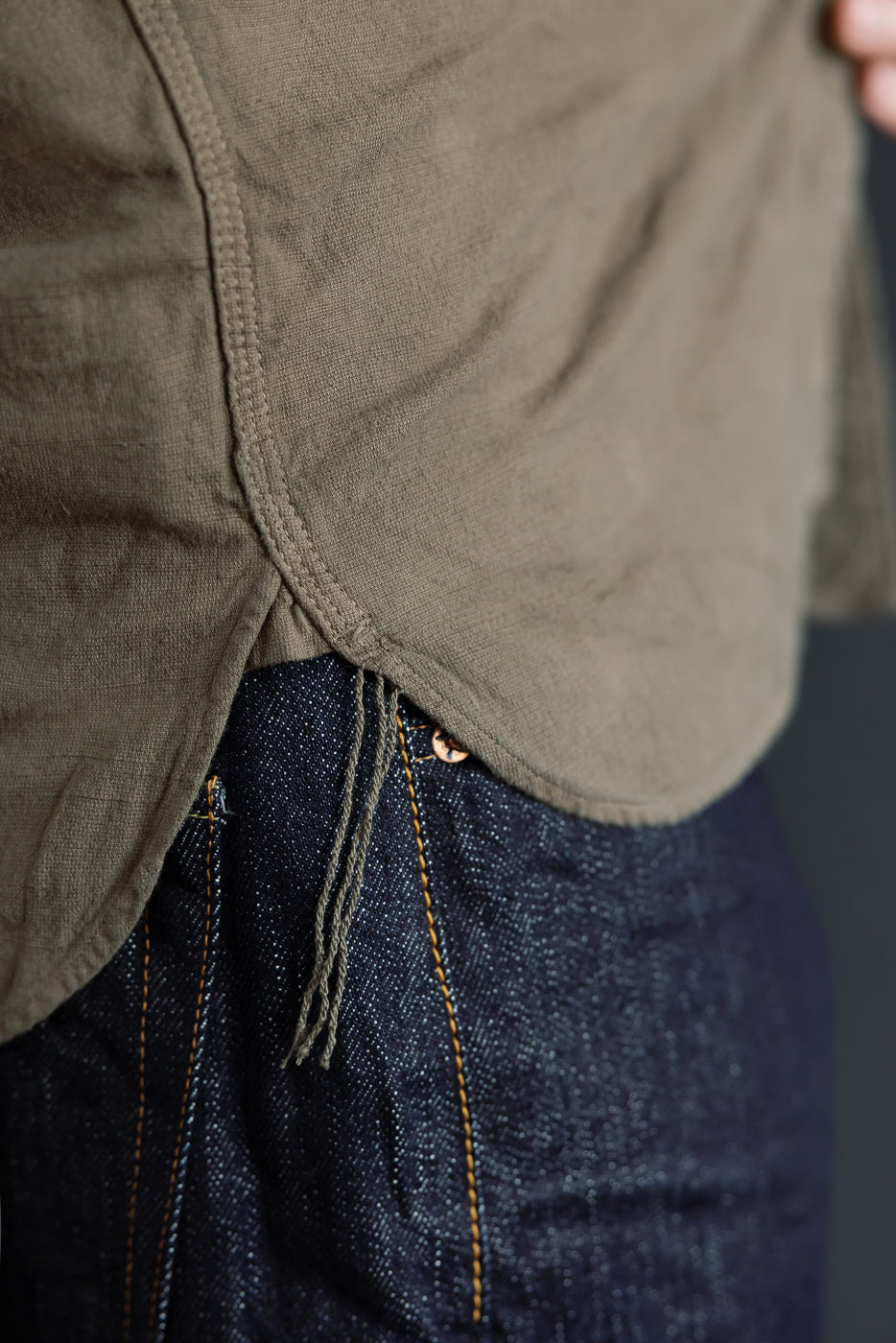 Close-up of olive shirt hem and selvedge denim jeans with orange stitching, front view