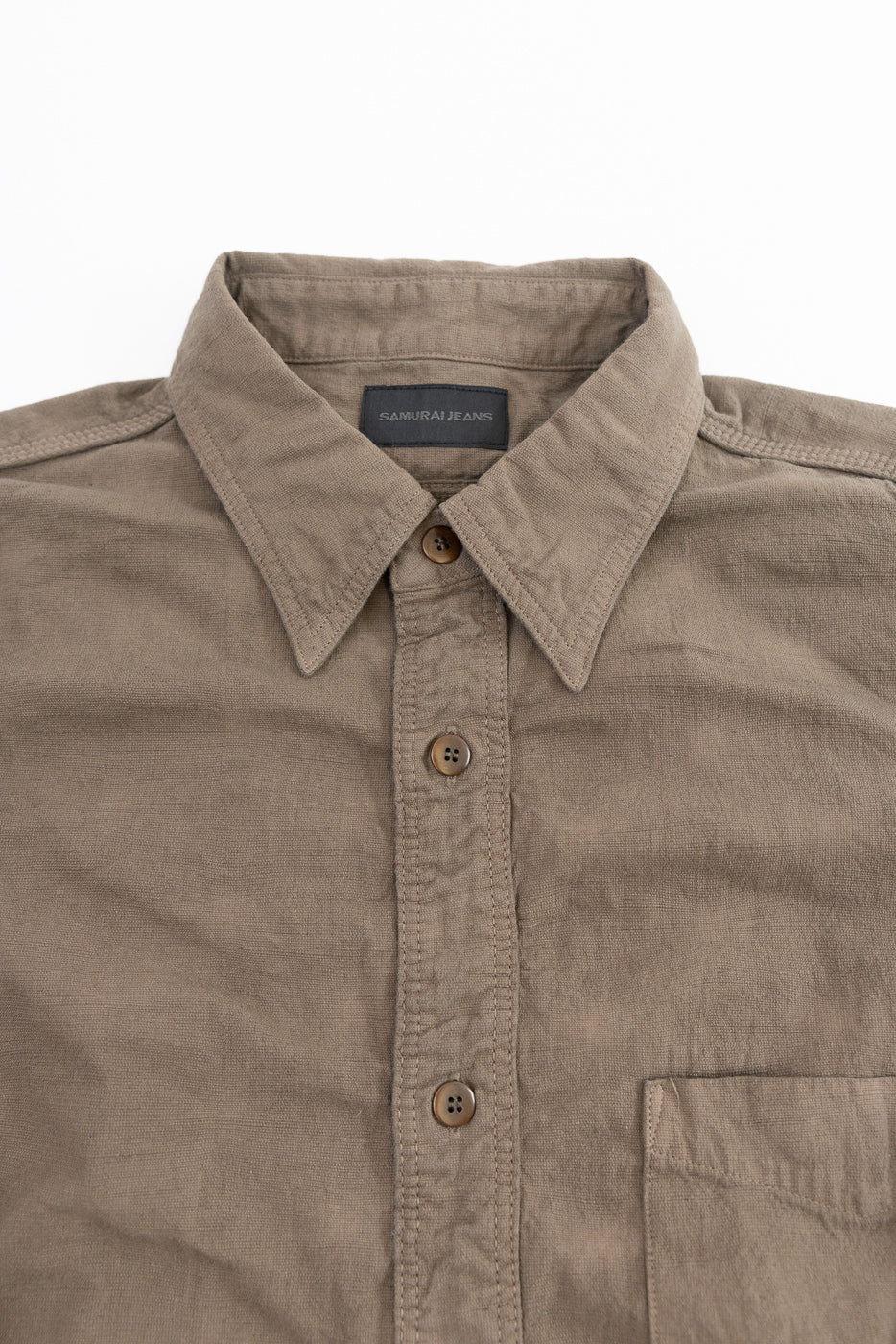 Close-up front view of olive button-up shirt, showing collar, SAMURAI JEANS tag, and chest pocket detail.