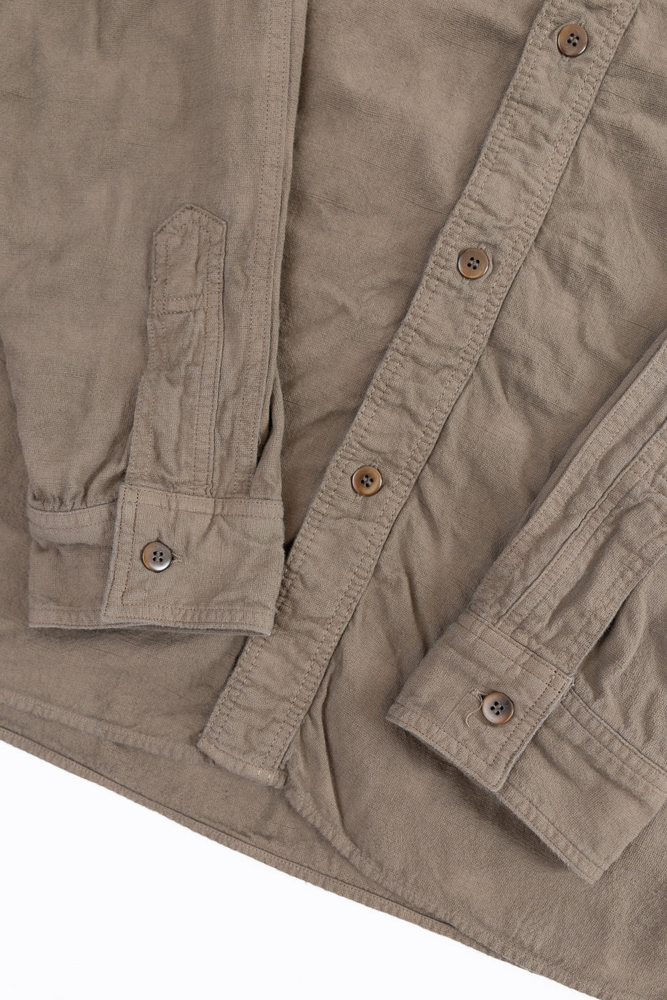 Close-up front view of tan button-up shirt showing chest pocket, button placket, and sleeve cuff details.