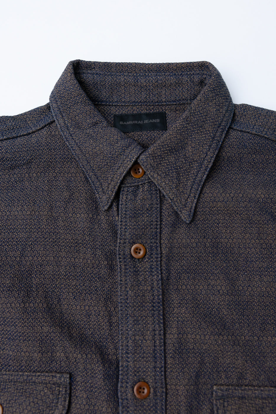 Close-up front view of dark textured shirt with button-down collar, brown buttons, and Samurai Jeans tag
