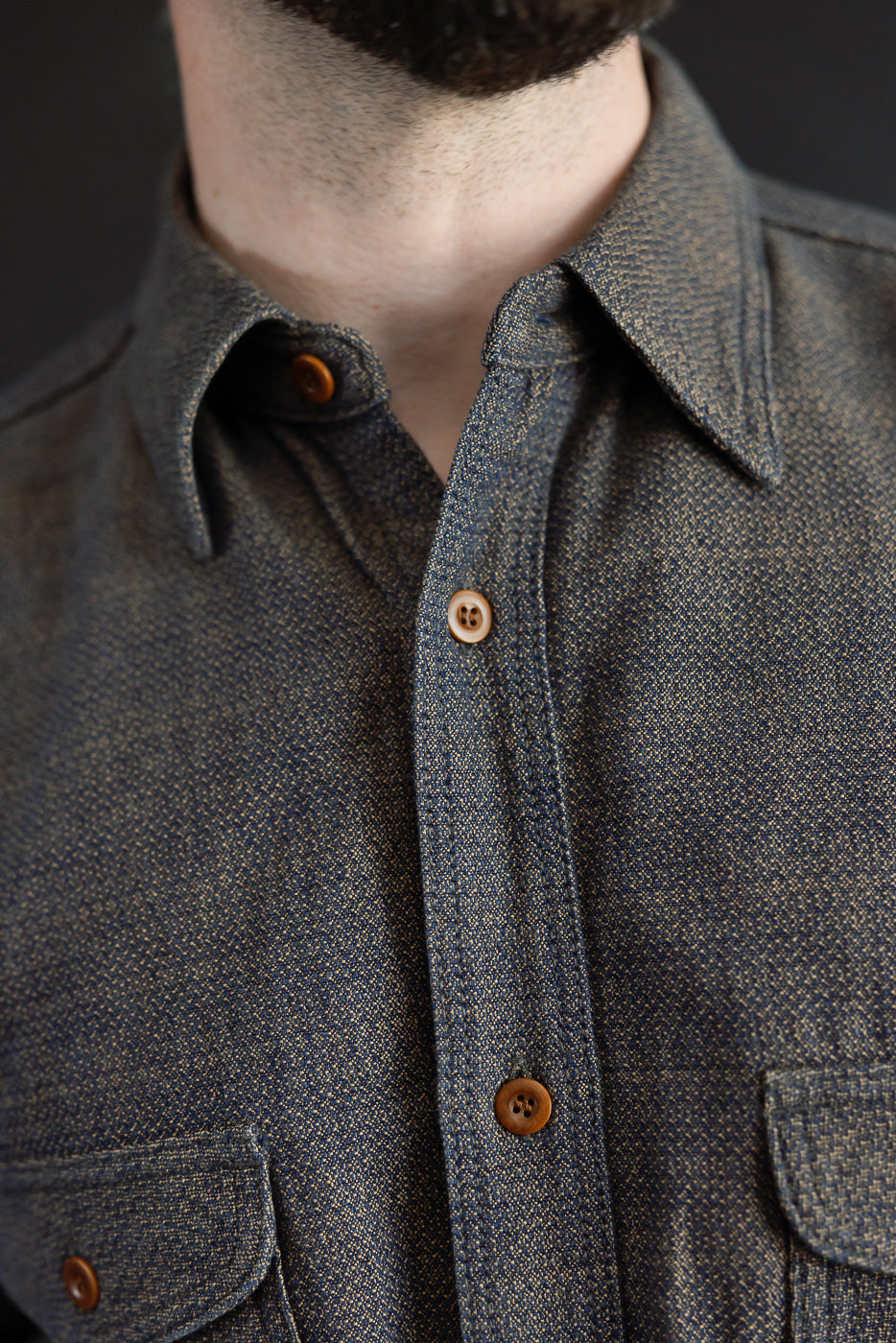 Close-up front view of male model wearing textured denim shirt with button-down collar, chest pockets, and brown buttons