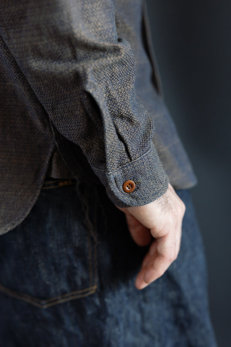 Close-up of male model's shirt sleeve, showcasing button detail and textured fabric, front view
