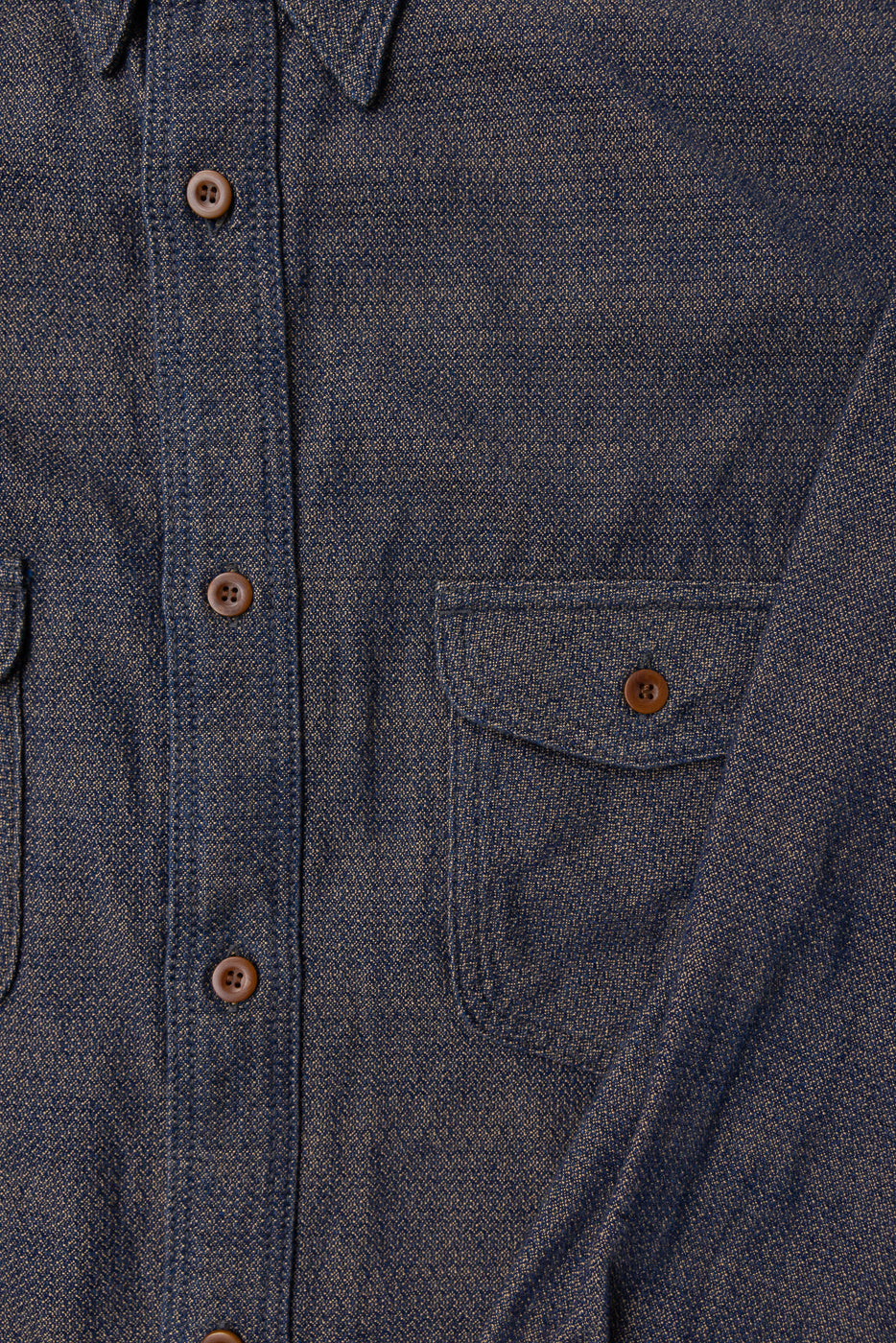 Close-up front view of dark denim shirt with brown buttons, chest pocket, and textured selvedge fabric detail.