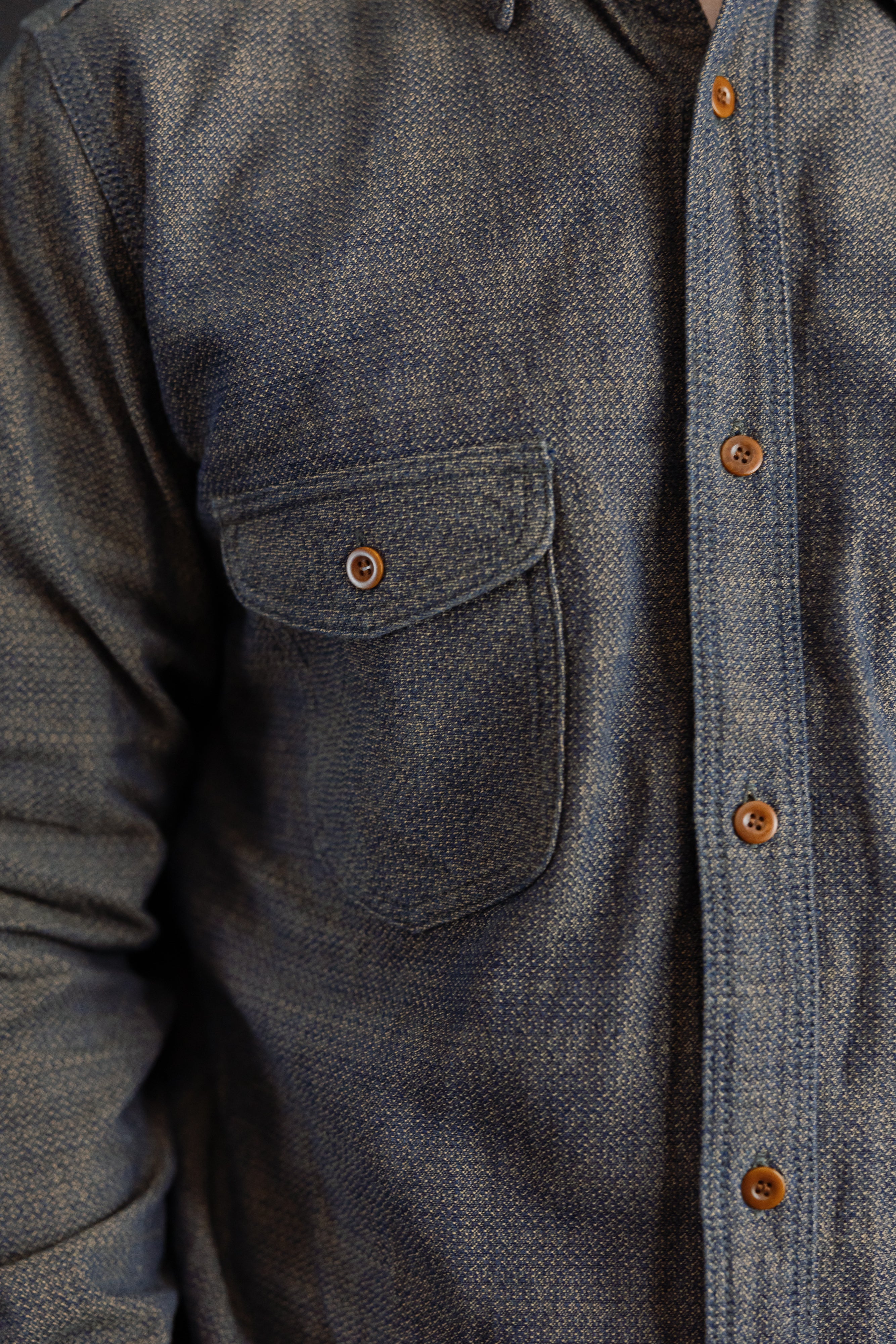 Close-up front view of men's textured chambray shirt showing chest pocket with button, button placket, and fabric weave detail.
