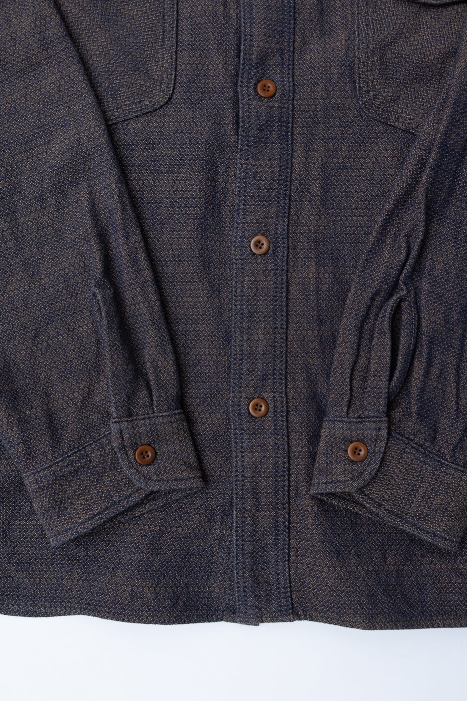 Close-up front view of dark selvedge shirt with brown buttons, chest pockets, and textured fabric weave