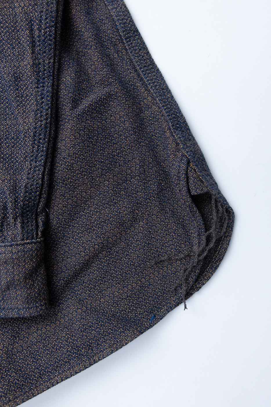 Close-up of selvedge denim shirt front, showcasing textured weave, button placket, and raw hem detail