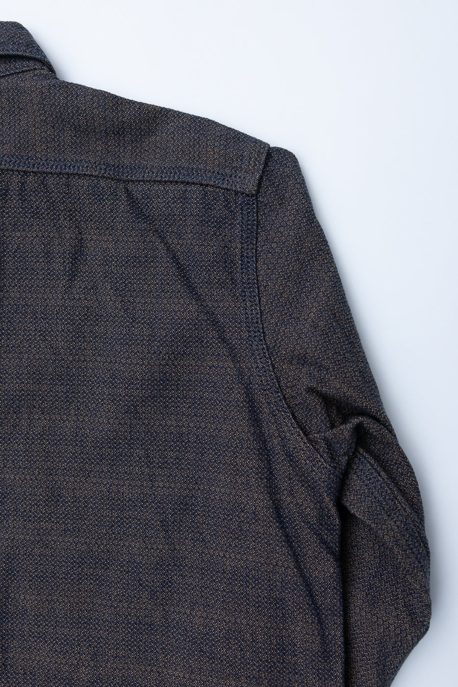 Close-up of dark selvedge shirt's shoulder and sleeve, showing textured fabric and tailored stitching detail