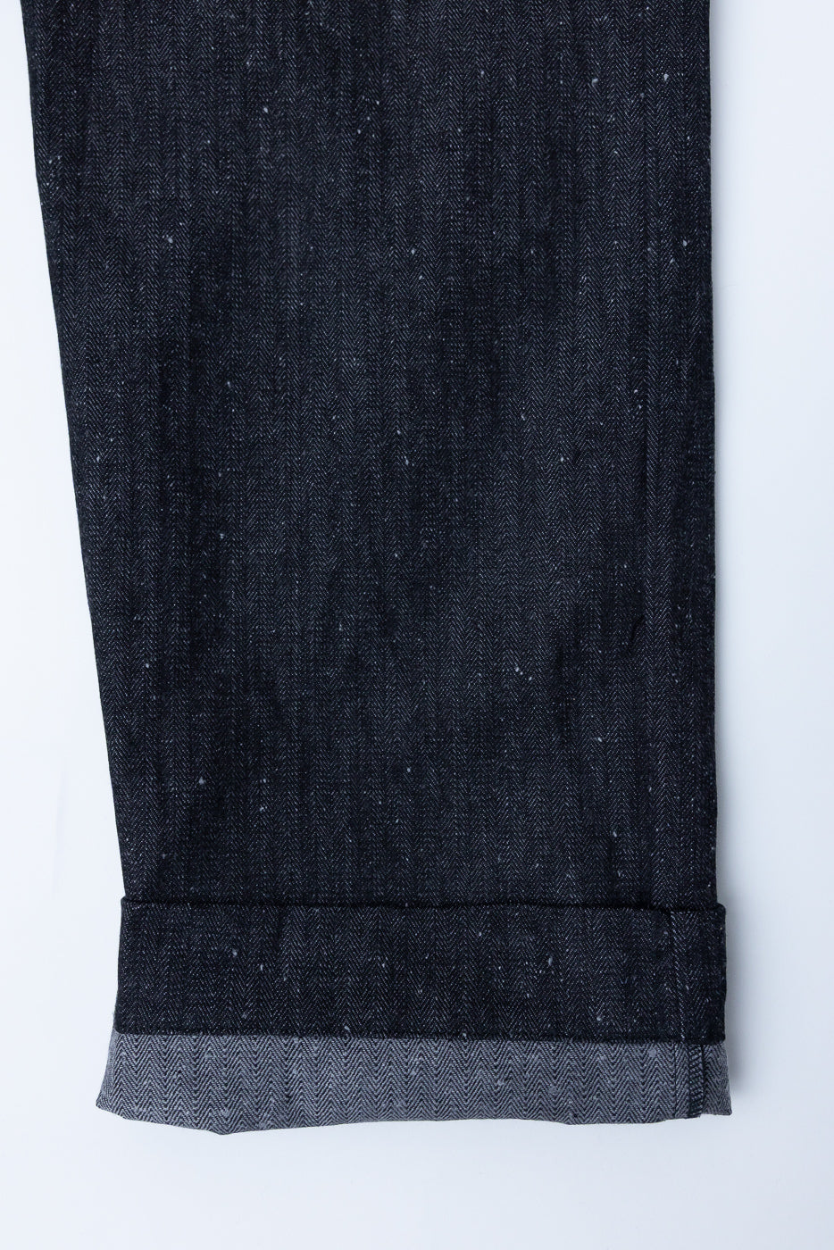 Close-up of dark selvedge denim pants hem, showcasing herringbone texture and folded cuff detail.