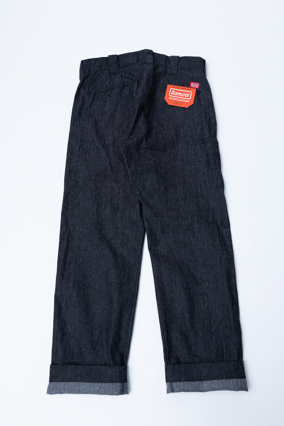 Back view flat lay of dark selvedge work pants with rolled cuffs, Samurai tag visible, showcasing fabric texture and rear pockets.