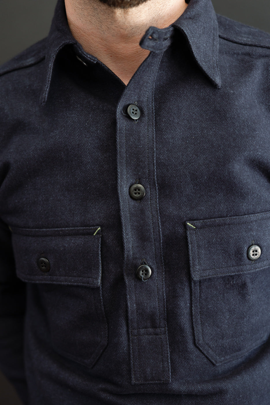 Close-up front view of dark denim shirt with buttons, chest pockets, and collar on male model