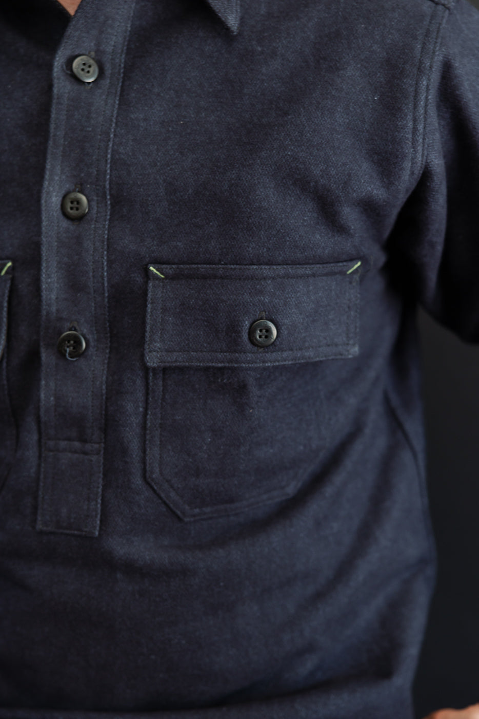 Close-up front view of dark denim shirt with buttoned chest pocket, worn by male model.