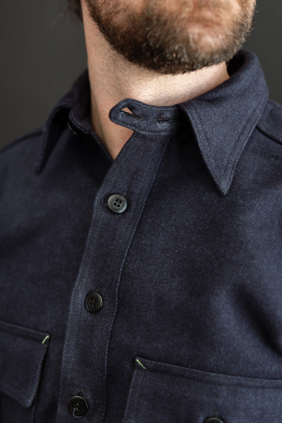 Close-up front view of navy shirt collar, buttons, and chest pockets on male model, 5'9