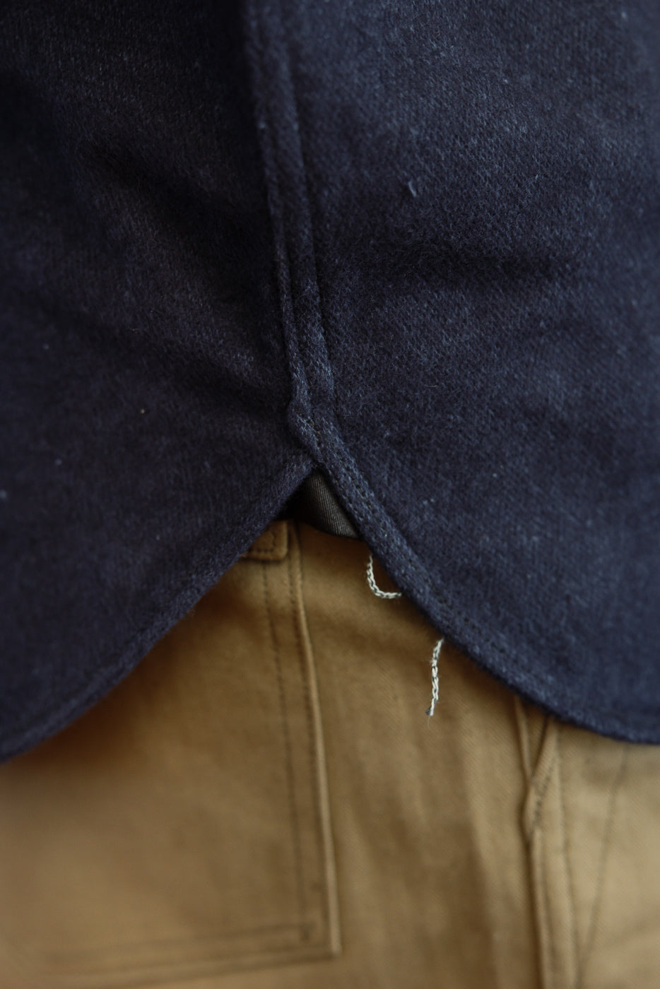 Close-up of dark navy shirt hem with raw selvedge edge, worn over tan pants, front view