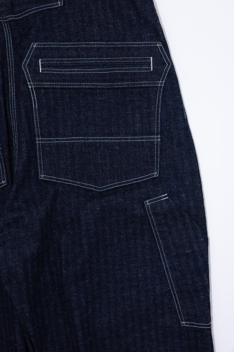 Close-up back view of dark selvedge denim jeans showing rear pocket with white contrast stitching and fabric texture