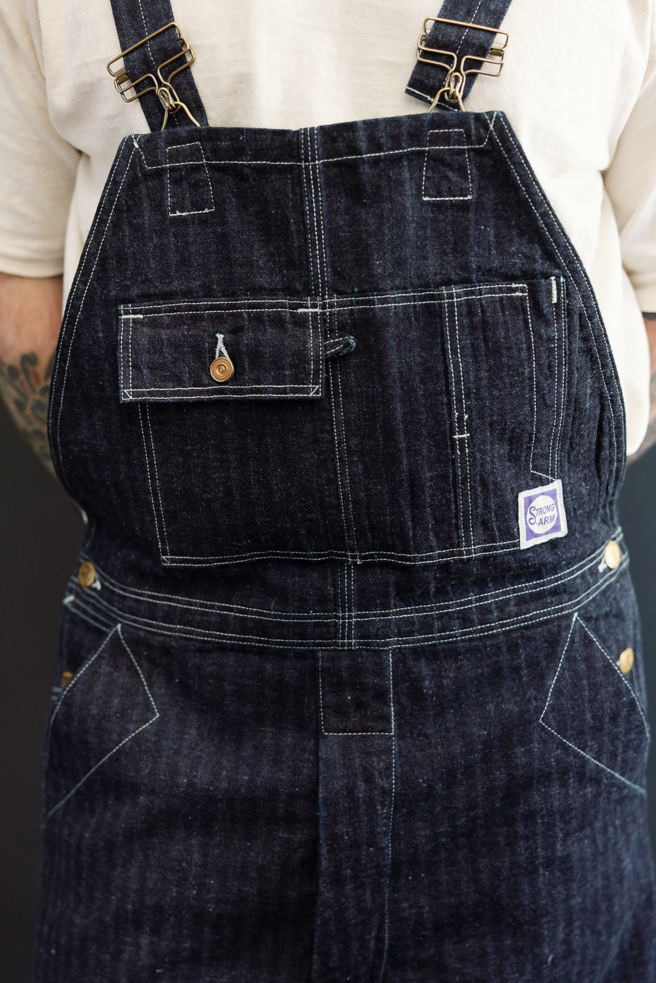 Front close-up of dark denim overalls on male model, 5'9