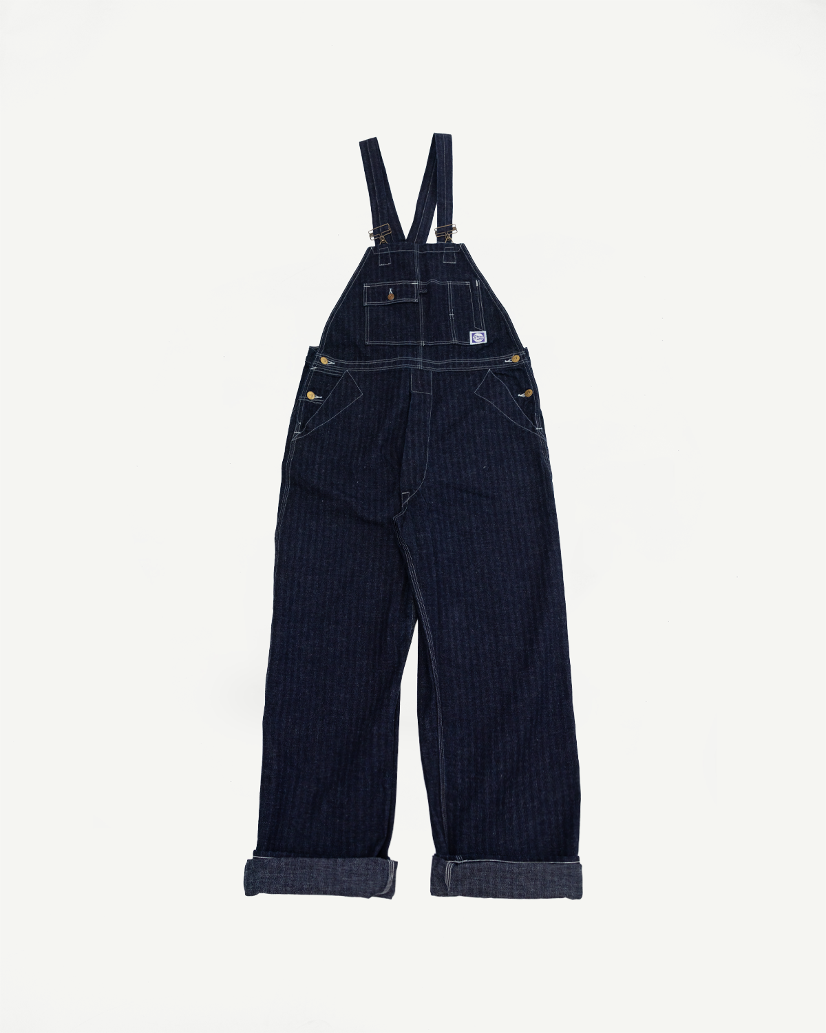 Front view of dark denim overalls with brass buttons, chest pocket, and cuffed hems; flat lay