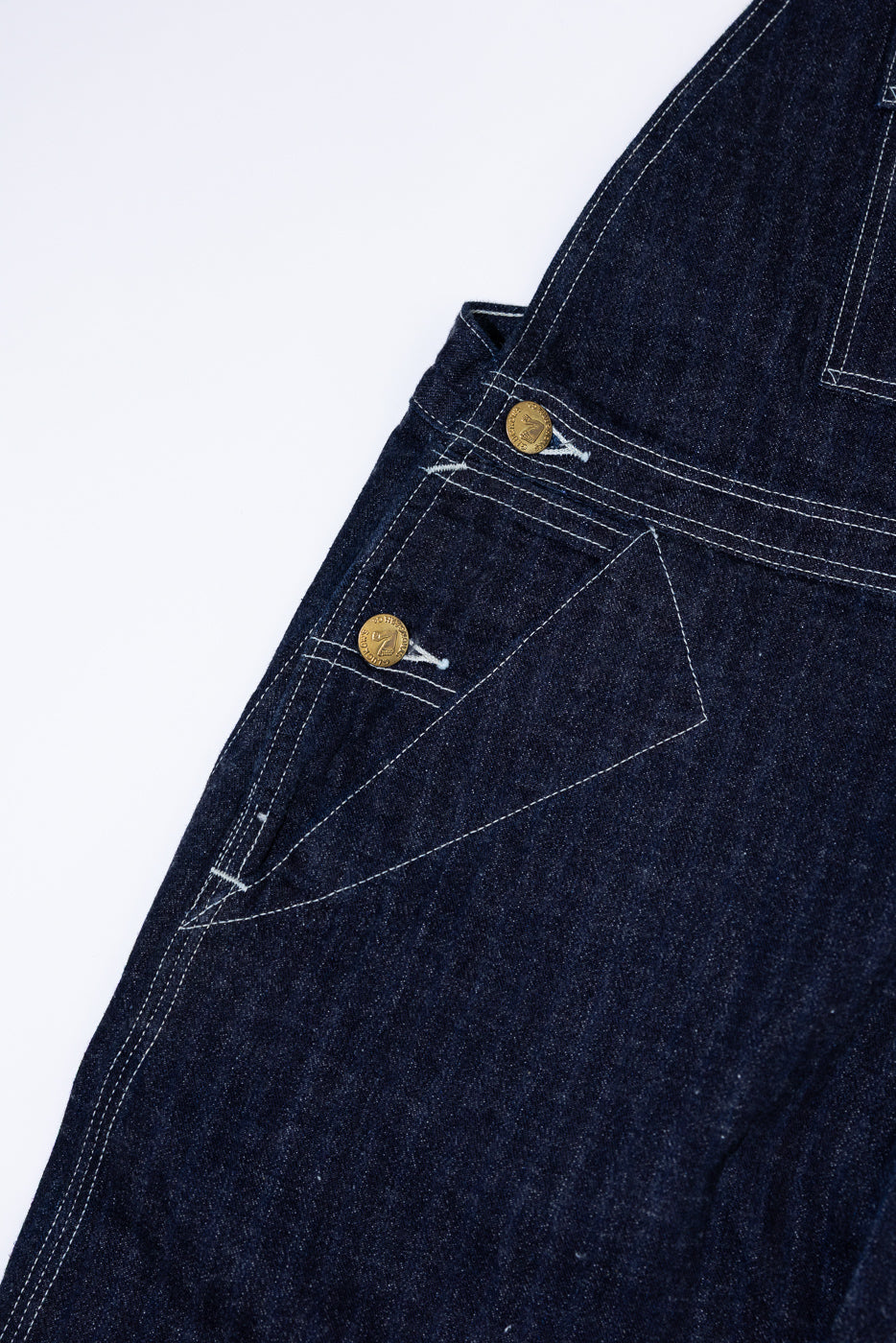 Close-up front view of dark selvedge denim jeans, showing gold buttons and white contrast stitching on pocket.