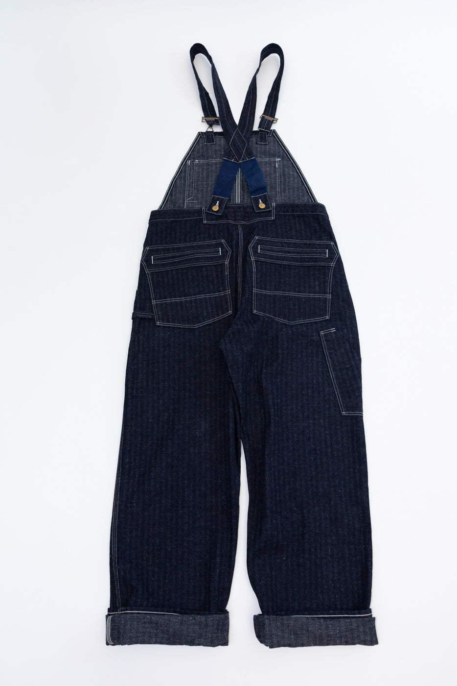 Back view of dark denim overalls with rolled hems, dual rear pockets, and adjustable straps