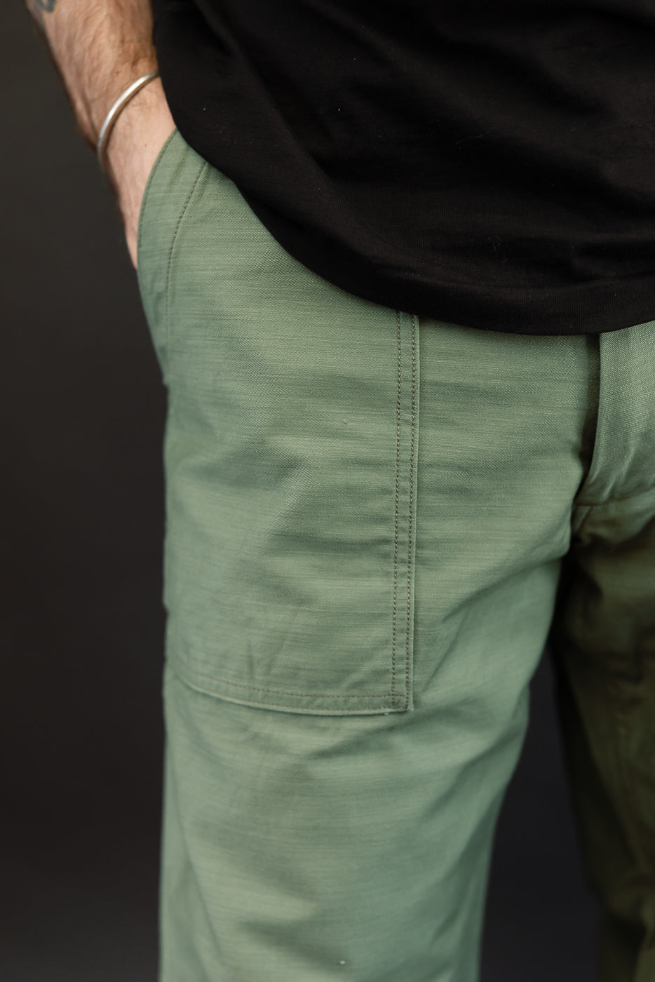 Close-up of male model's side, showing olive green cargo pants with visible pocket stitching and fabric texture.