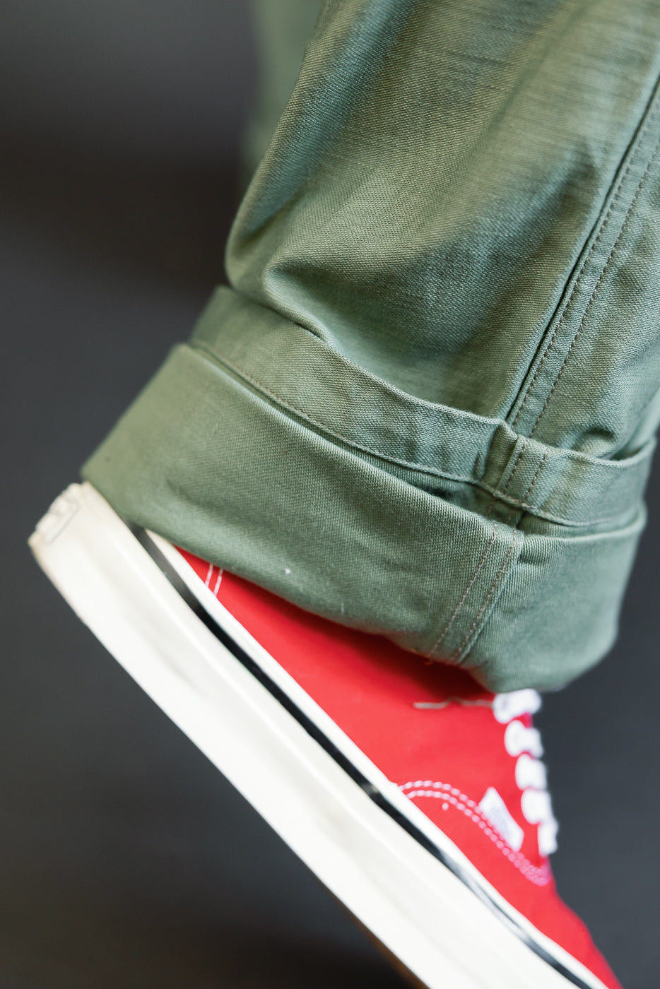 Close-up of olive green pants cuff, showing hem detail and texture, paired with red sneaker