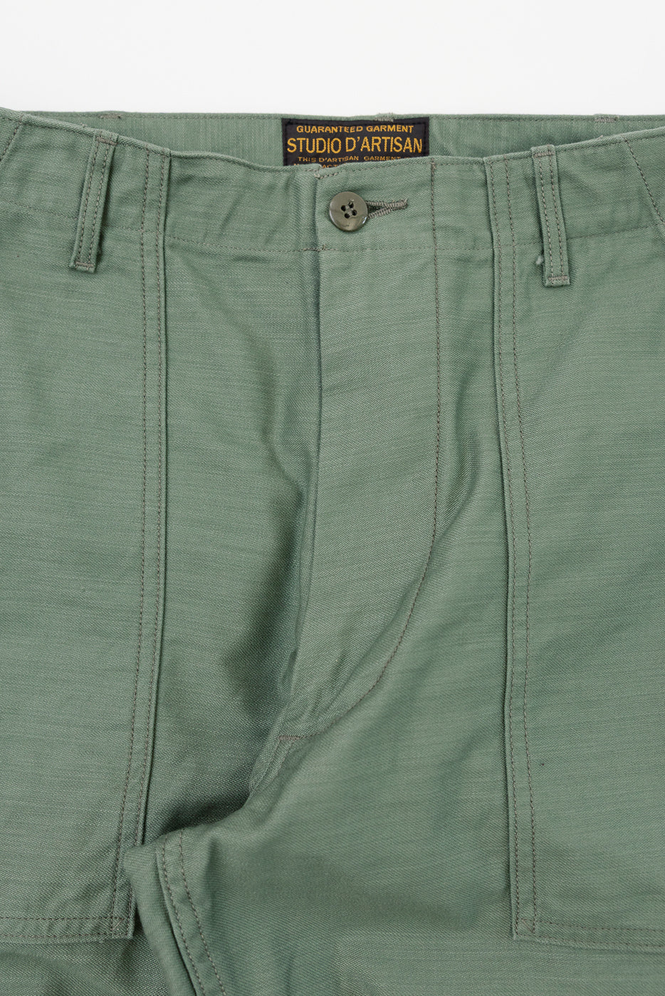 Close-up front waistband of olive green men's chinos, showing button closure, stitching, and Studio D'Artisan label