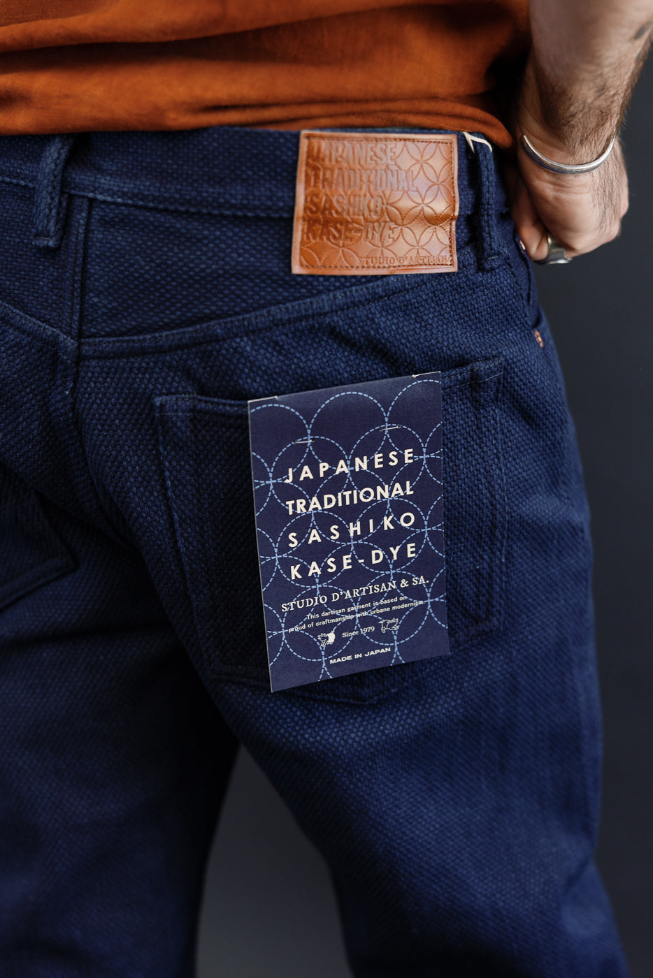 Close-up of back of men's selvedge jeans, showcasing leather patch and tag details, athletic build model.