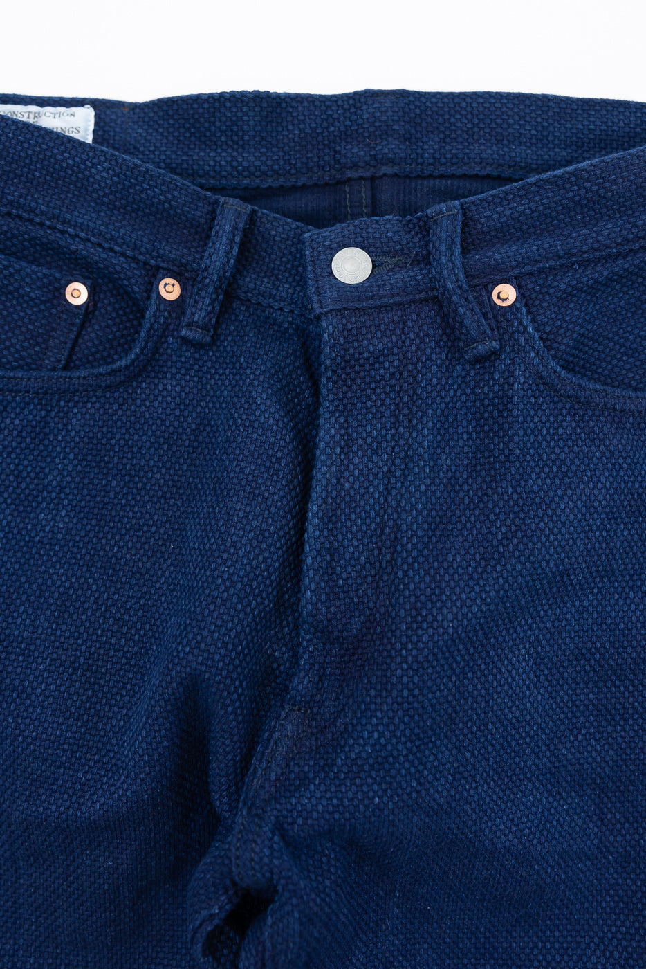 Close-up front view of dark blue selvedge jeans with copper rivets and button fly detail