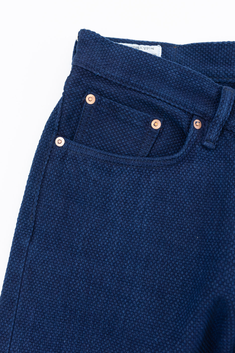 Close-up front view of dark blue selvedge jeans with copper rivets and textured fabric
