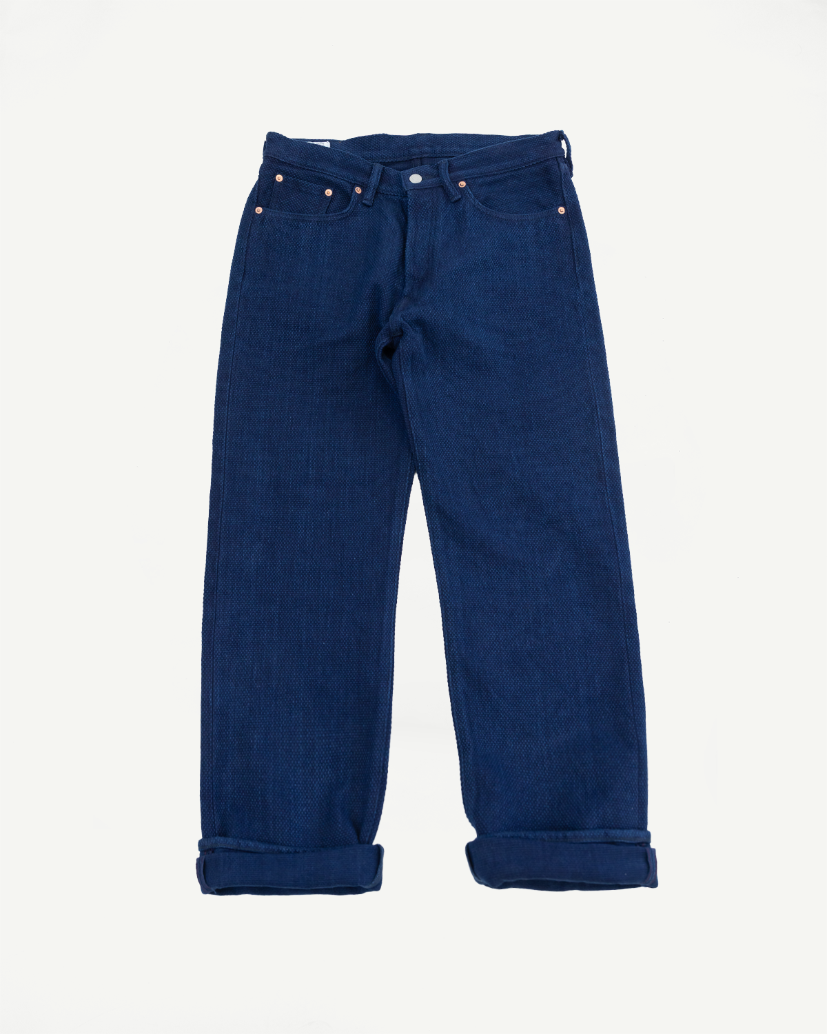 Front view of dark blue selvedge jeans with copper rivets, cuffed hems, and classic five-pocket design