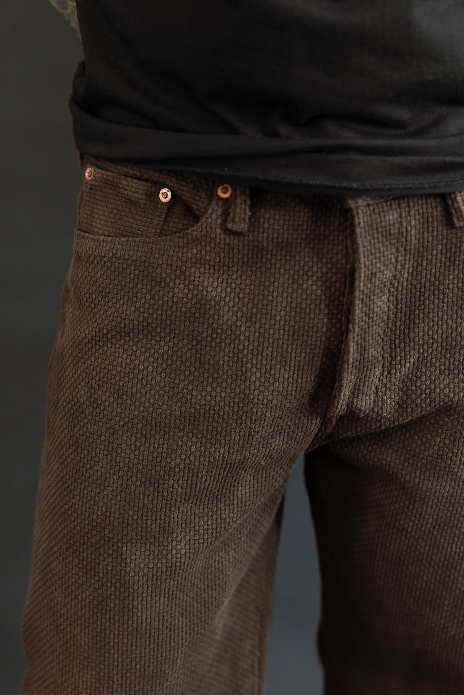 Close-up front view of brown corduroy pants with copper buttons, worn by male model