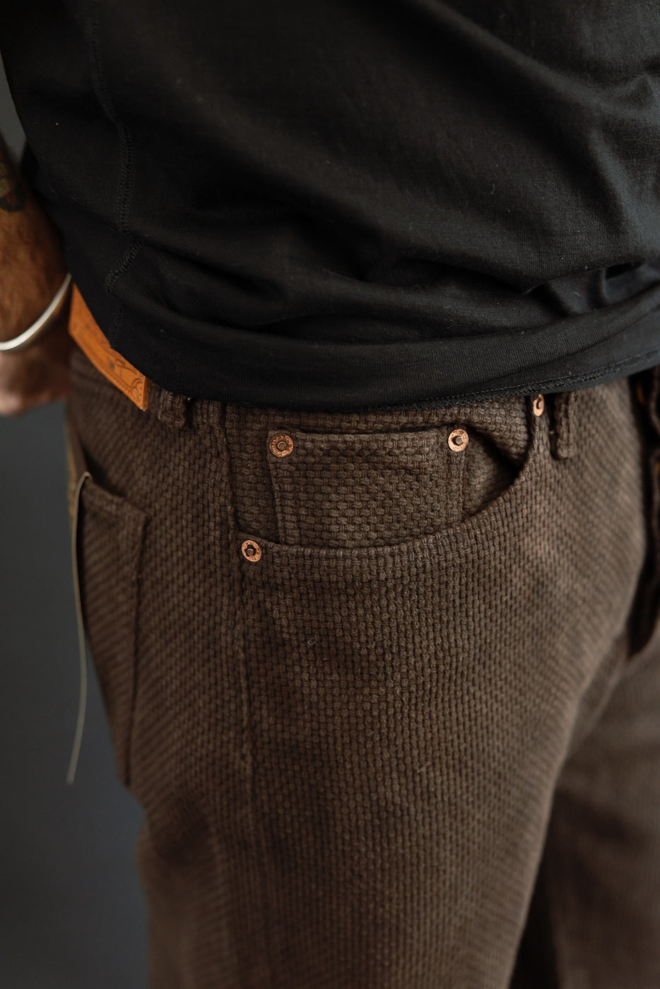 Close-up front view of brown waffle-knit pants with copper rivets, worn by male model, 5'9