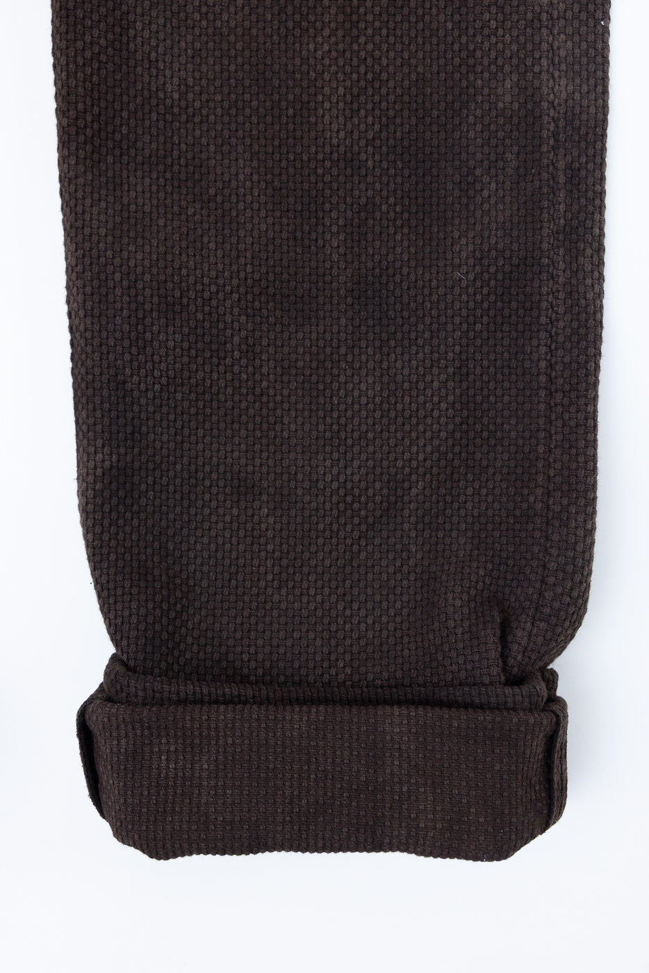 Close-up front view of dark brown textured pants with cuffed hem, showcasing fabric weave detail