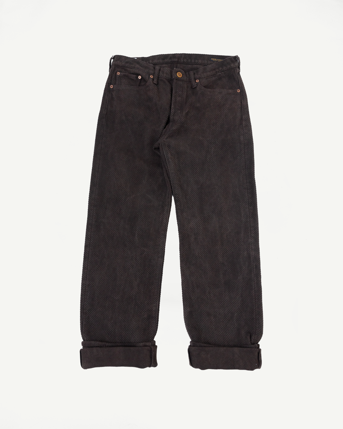 Flat lay front view of dark selvedge corduroy pants with cuffed hems, copper rivets, and button fly