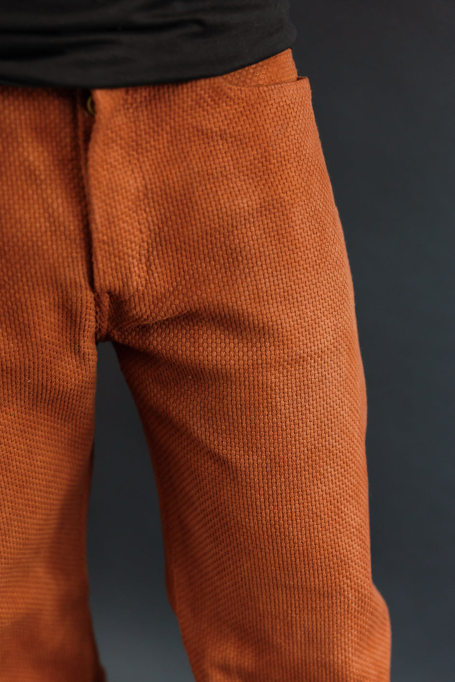 Close-up front view of rust orange textured pants on male model, 5'9