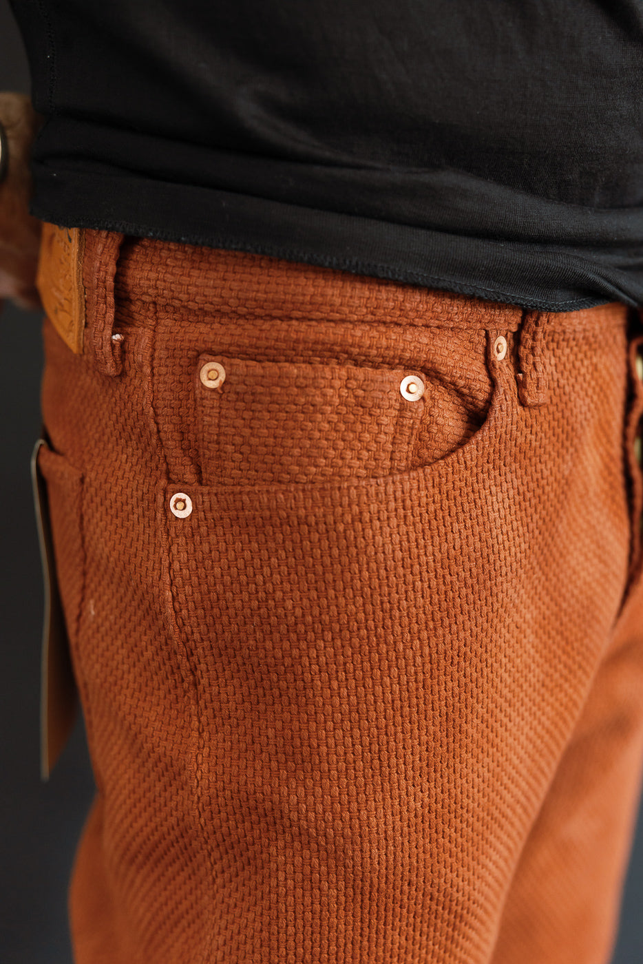 Close-up front view of rust corduroy pants with buttoned pockets, worn by male model, 5'9
