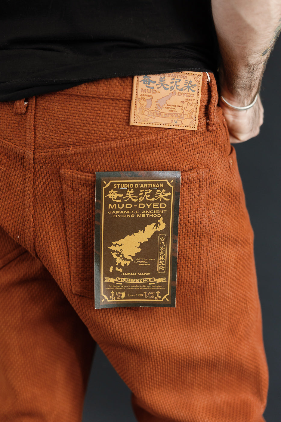 Close-up of male model's back pocket showing mud-dyed corduroy pants with tag details, athletic build