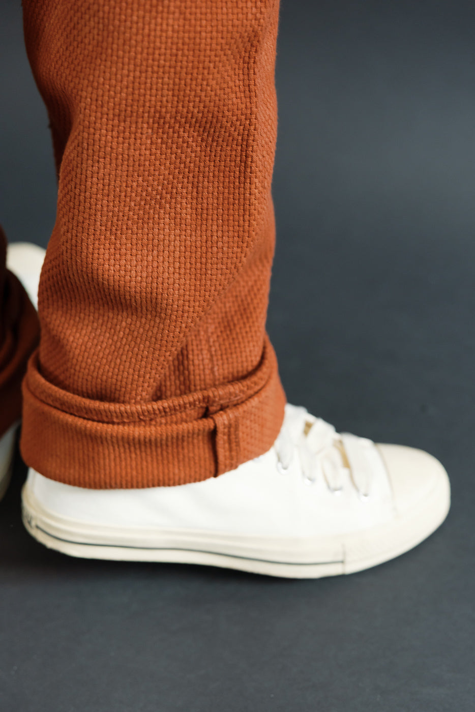 Close-up side view of male model's rust waffle knit pants cuff over white sneakers, athletic build