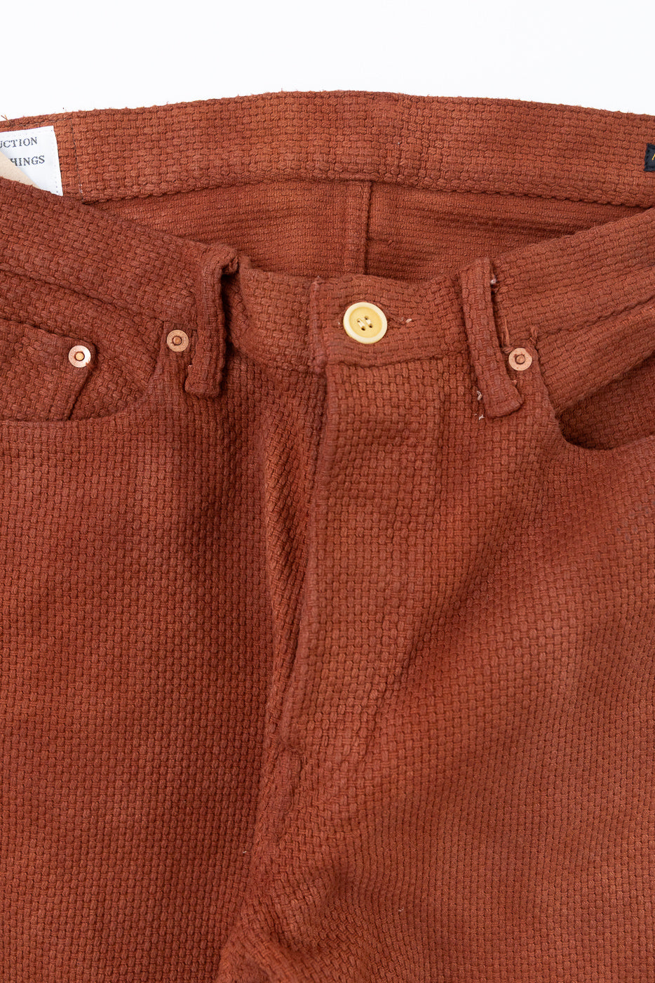 Close-up front view of rust-colored textured pants with button fly and belt loops