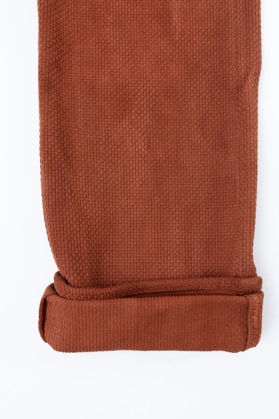 Close-up of rust-colored waffle knit pants hem, showcasing texture and rolled cuff detail