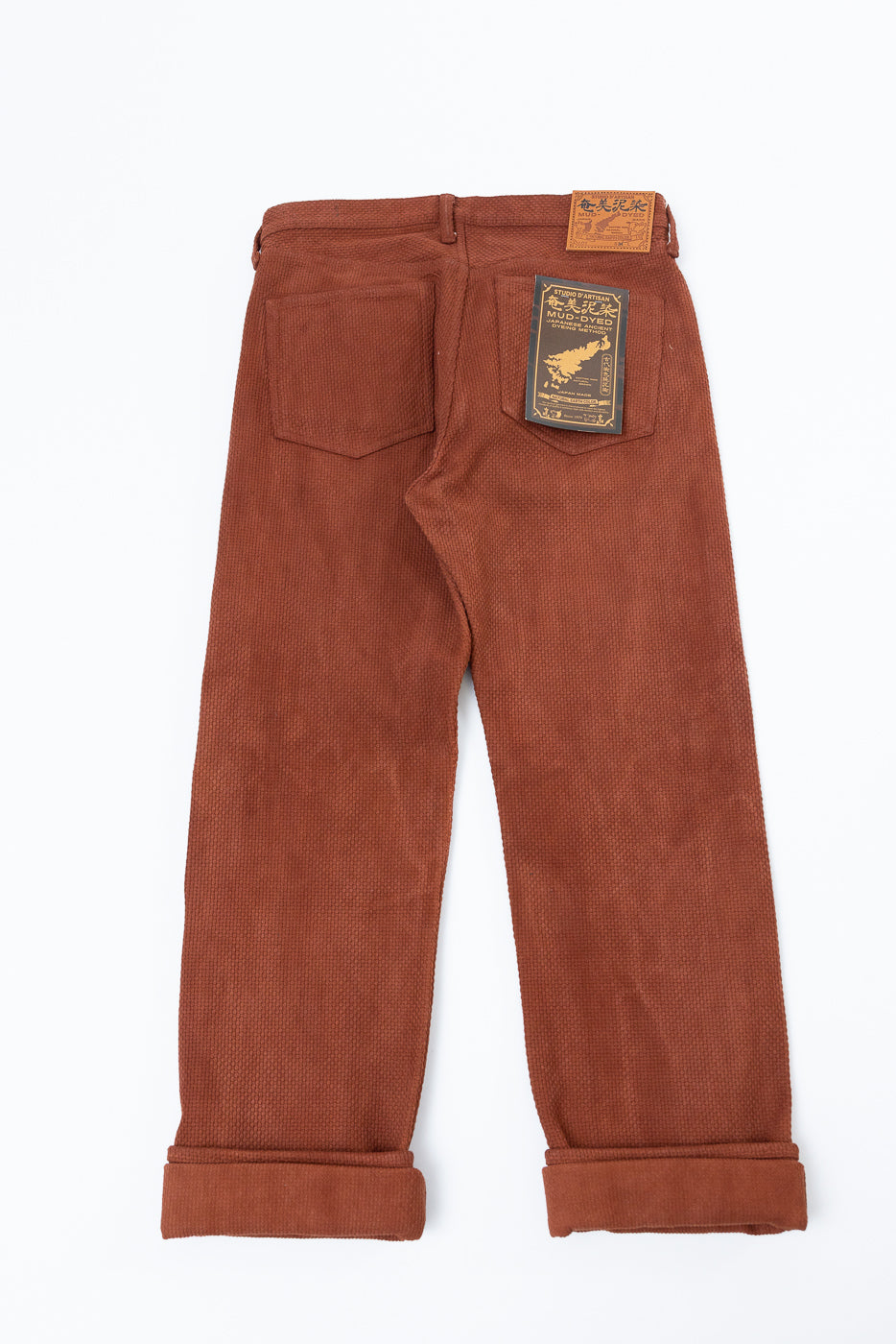 Back view of rust corduroy pants with rolled hems, back pocket tag, and waist label detail