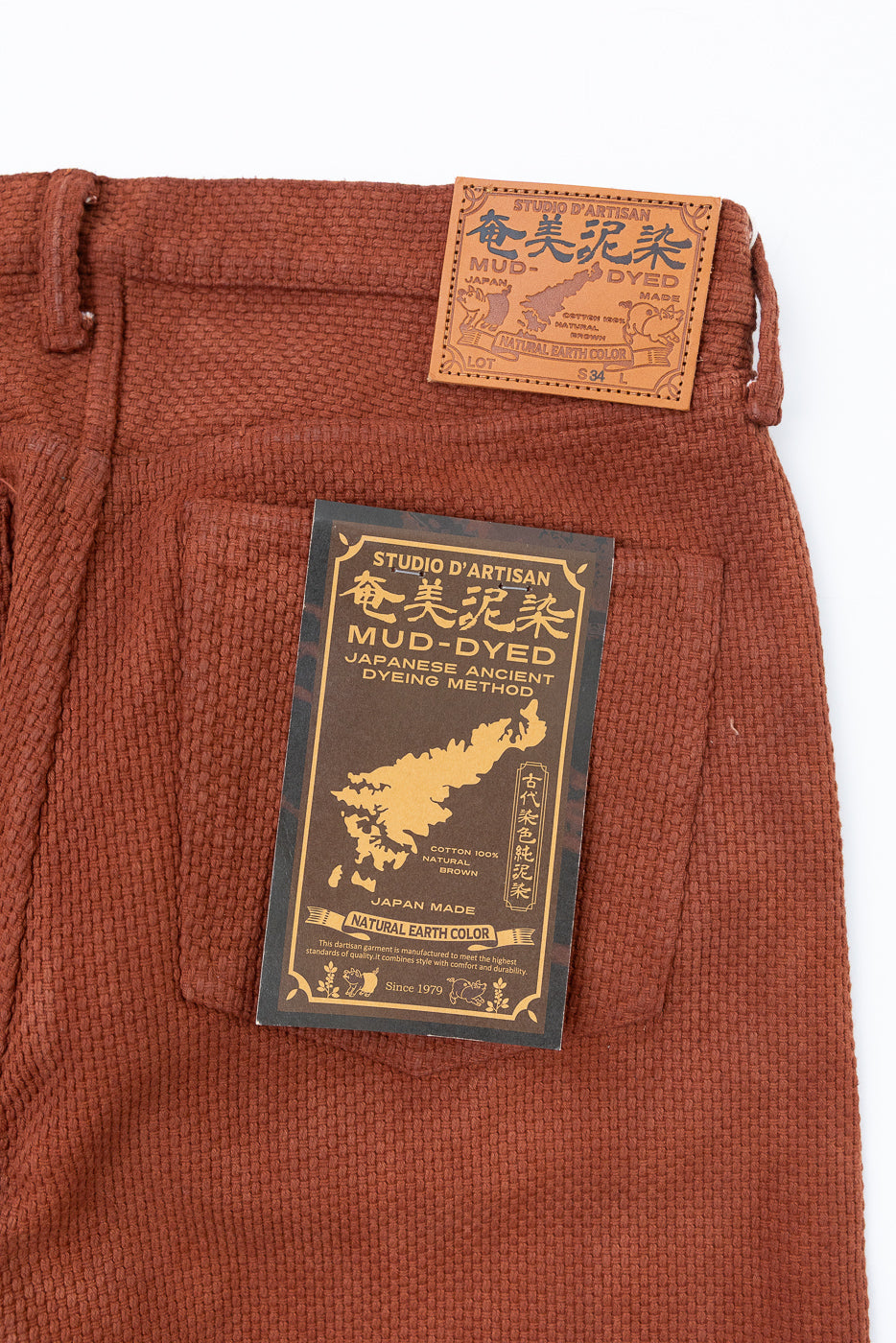 Close-up front view of mud-dyed brown cotton pants with leather patch & tag, Japanese artisan dyeing, natural earth color