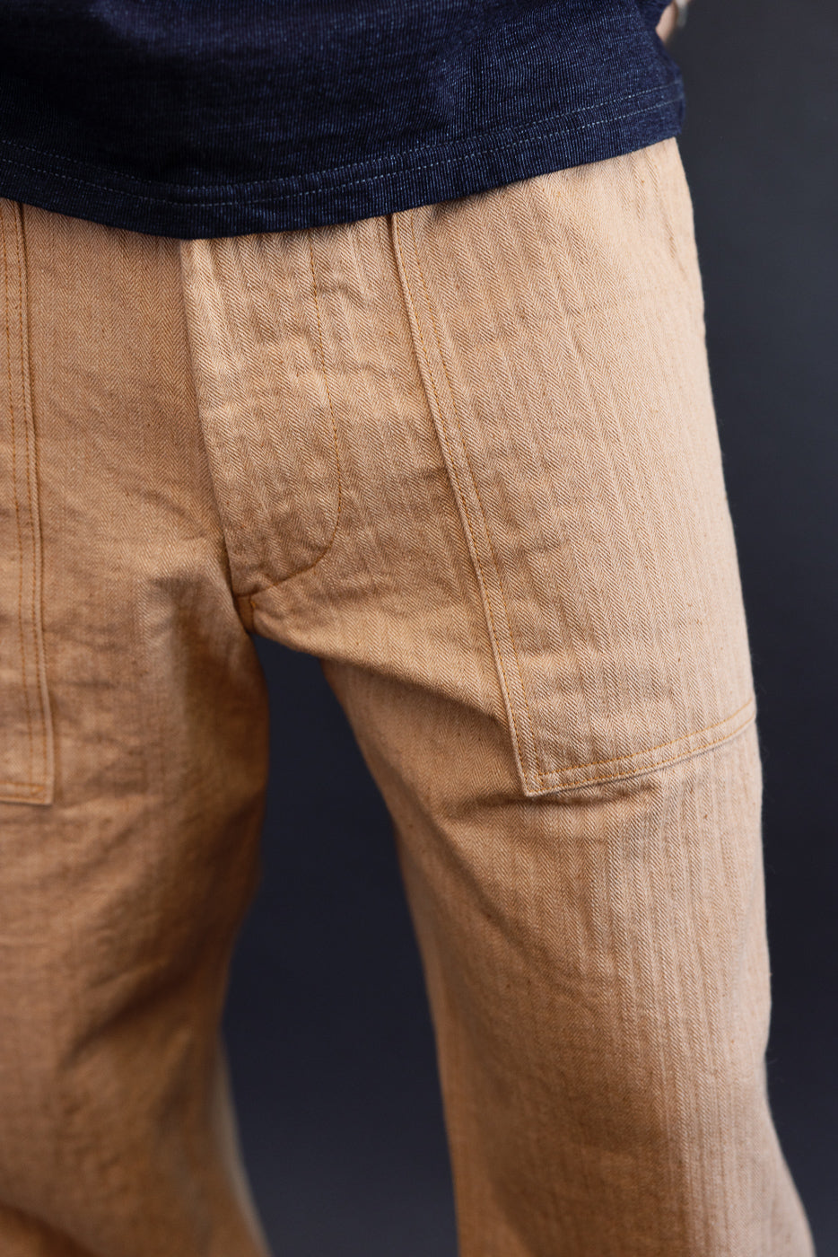 Close-up side view of tan herringbone cargo pants on male model, showing front pocket detail and fabric texture
