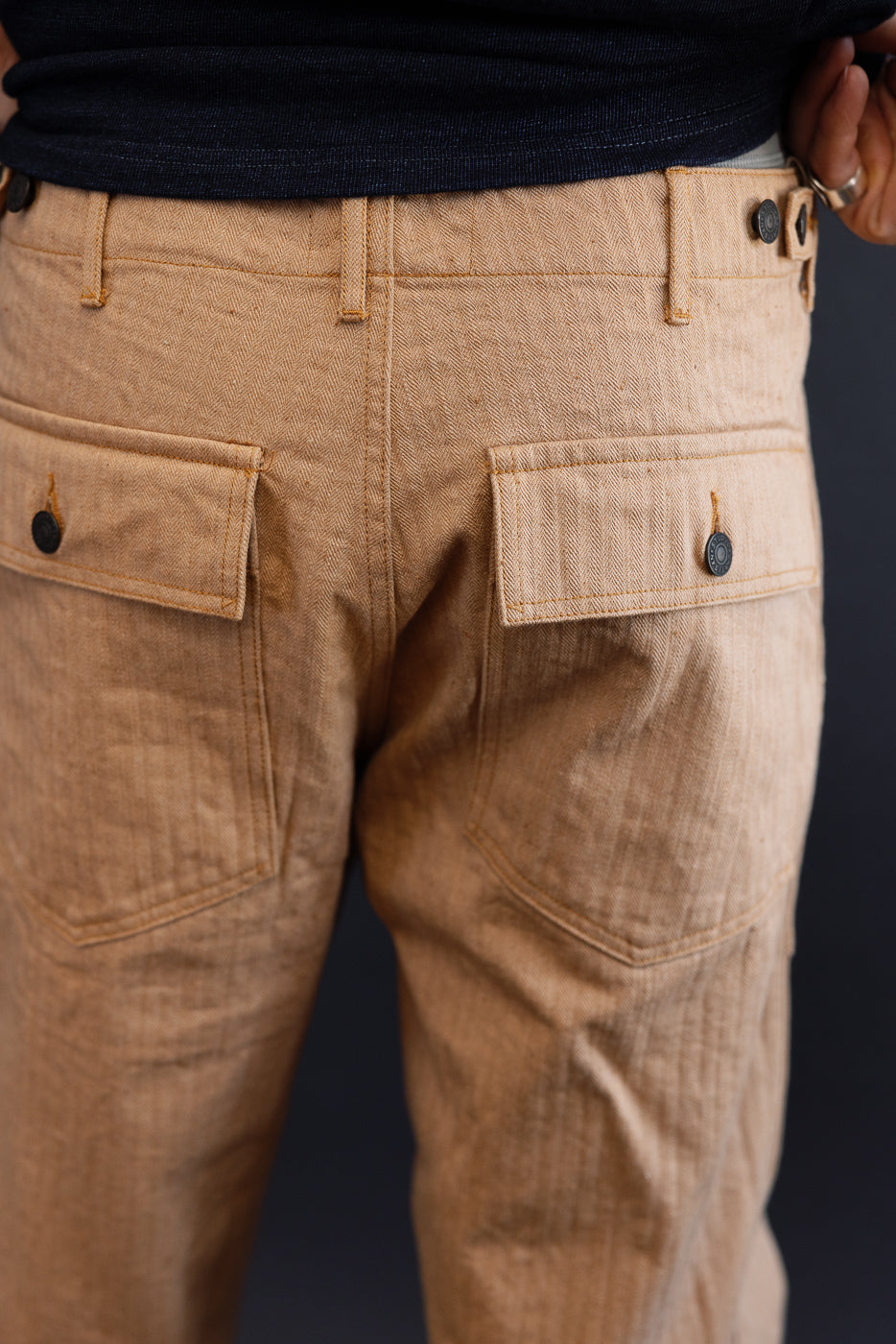 Back view of tan herringbone pants with buttoned pockets, worn by male model, 5'9