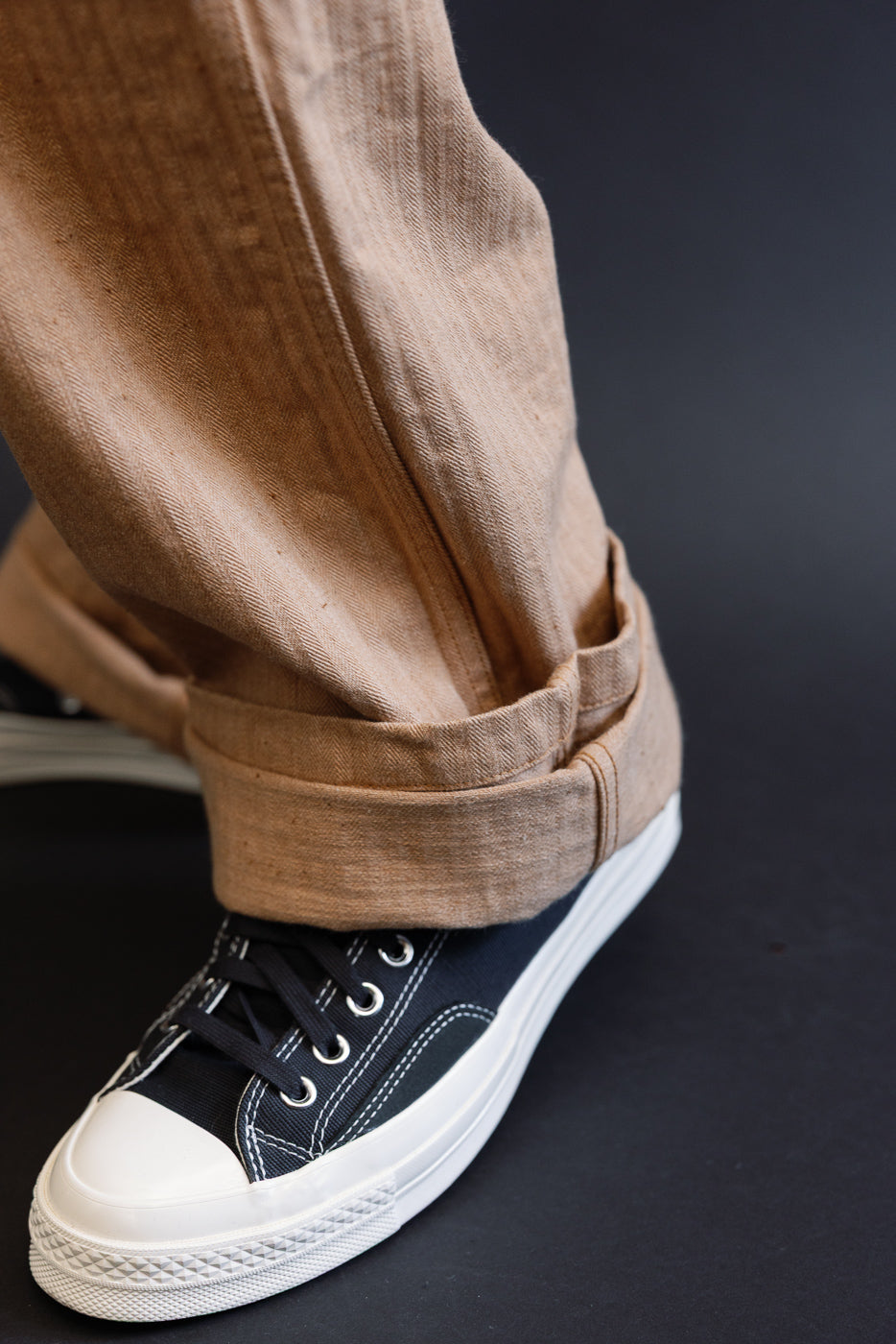 Close-up of male model's rolled hem on tan pants paired with black sneakers, front view