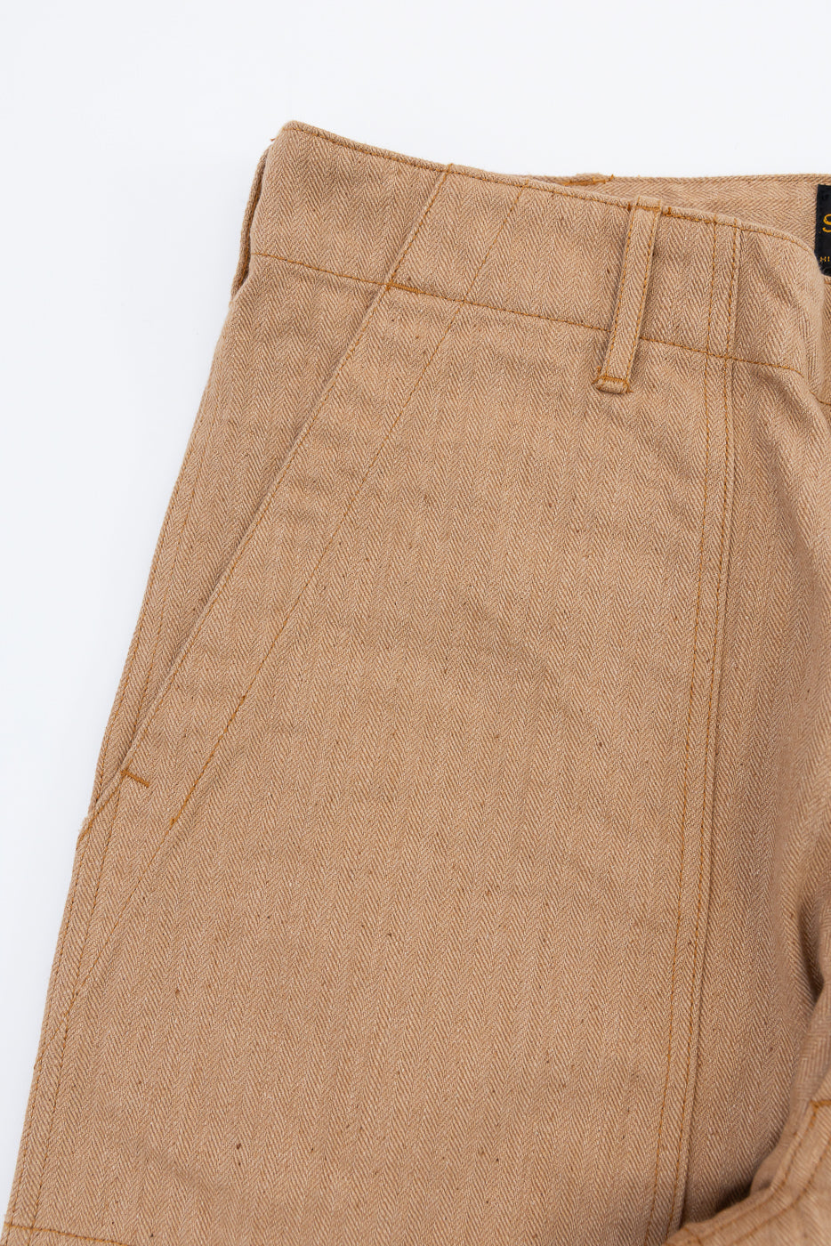 Close-up front view of tan herringbone chinos showing waistband, belt loops, and fabric texture